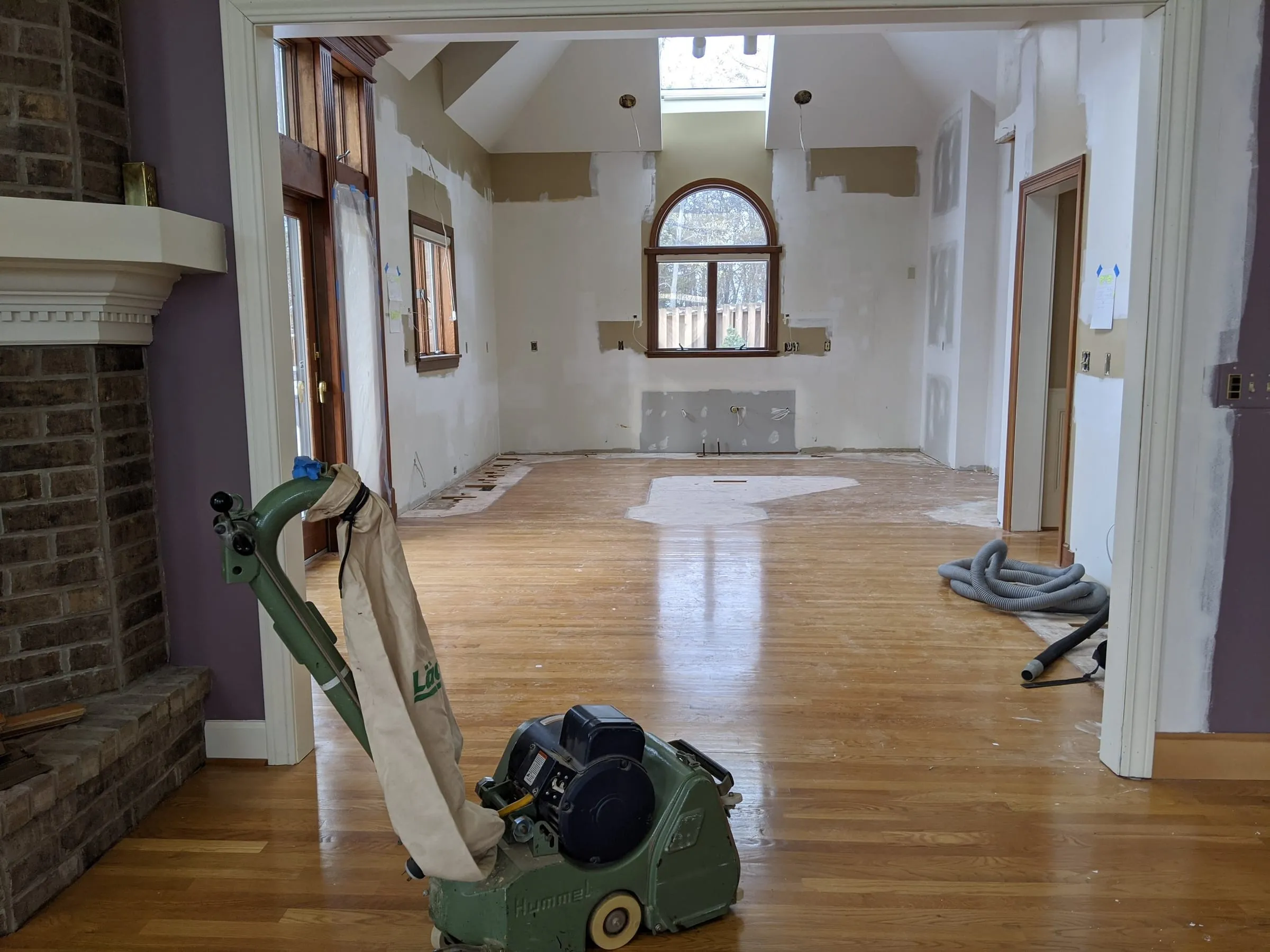Drum sander on a partly sanded oak floor in a living room with a brick fireplace