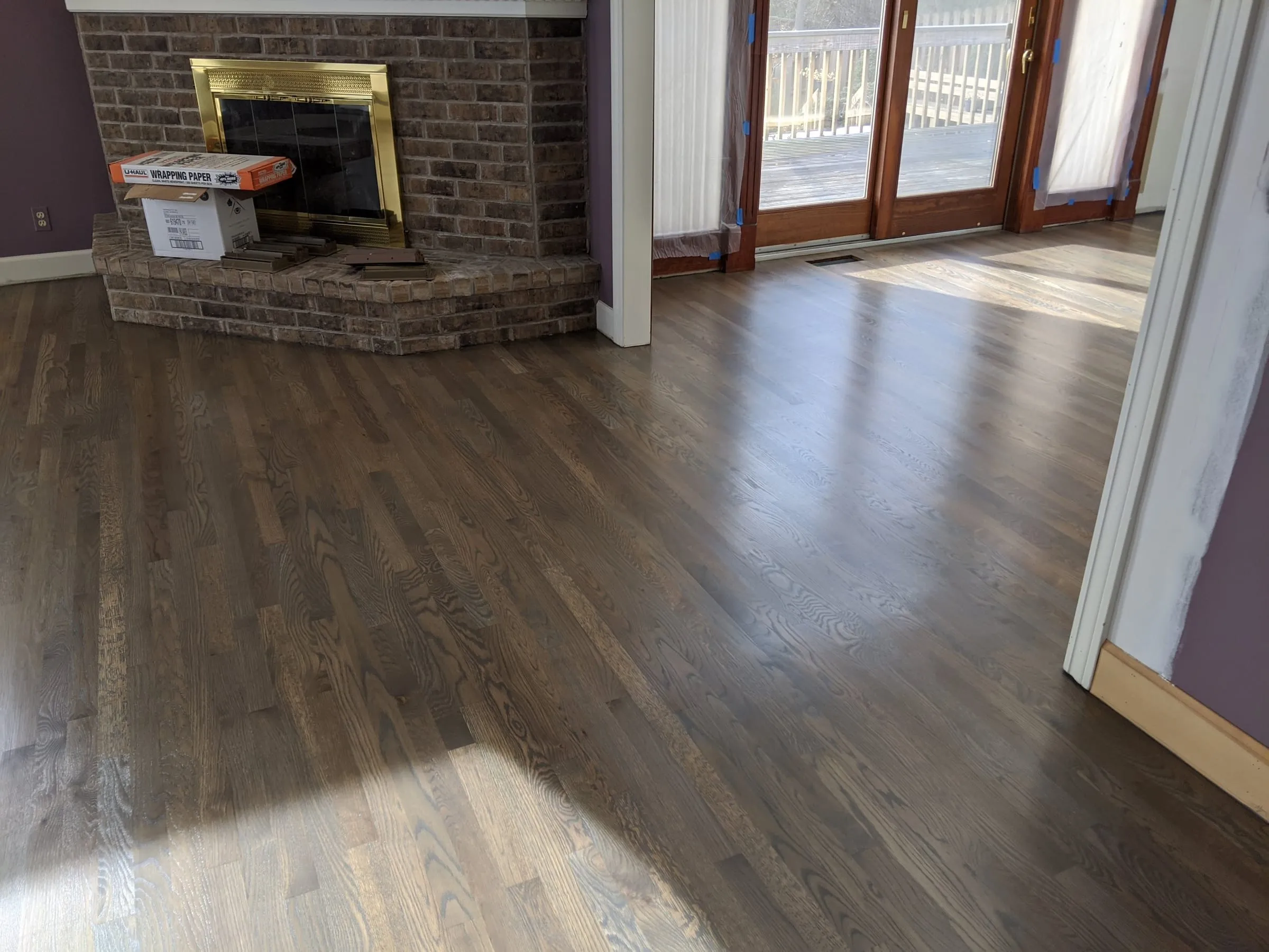 Sunlit gray-brown oak floor by a fireplace and patio doors