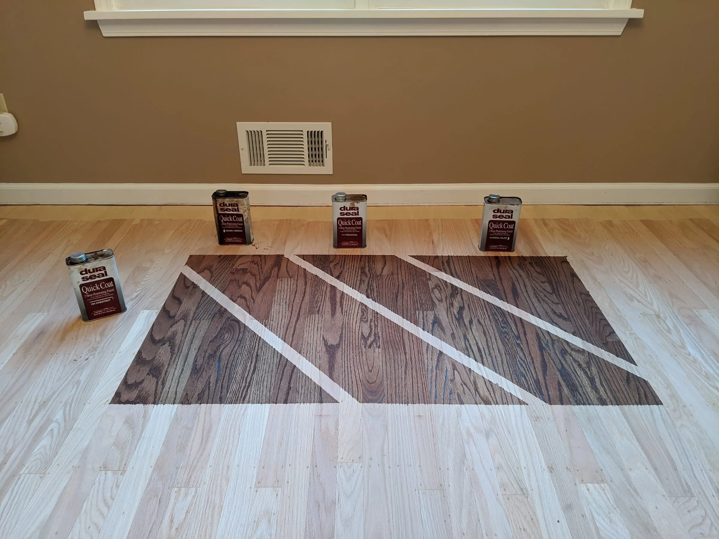 Stain samples applied to a sanded oak floor beside cans of finish