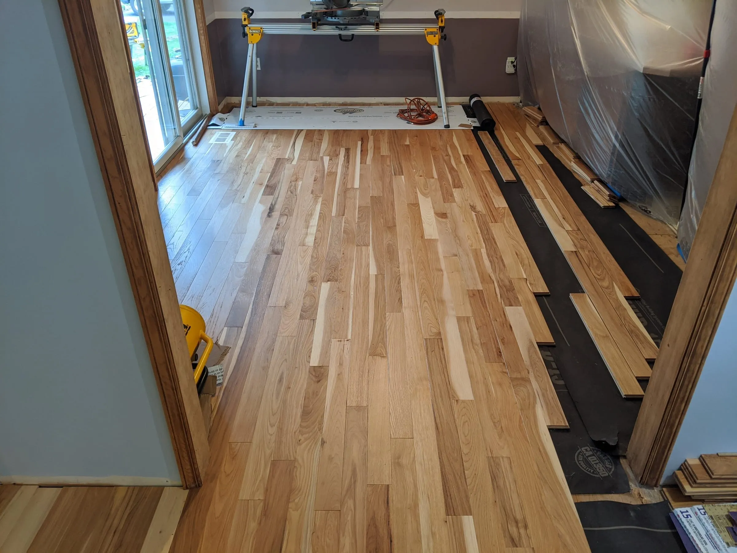 New hickory flooring being installed in a room with plastic sheeting