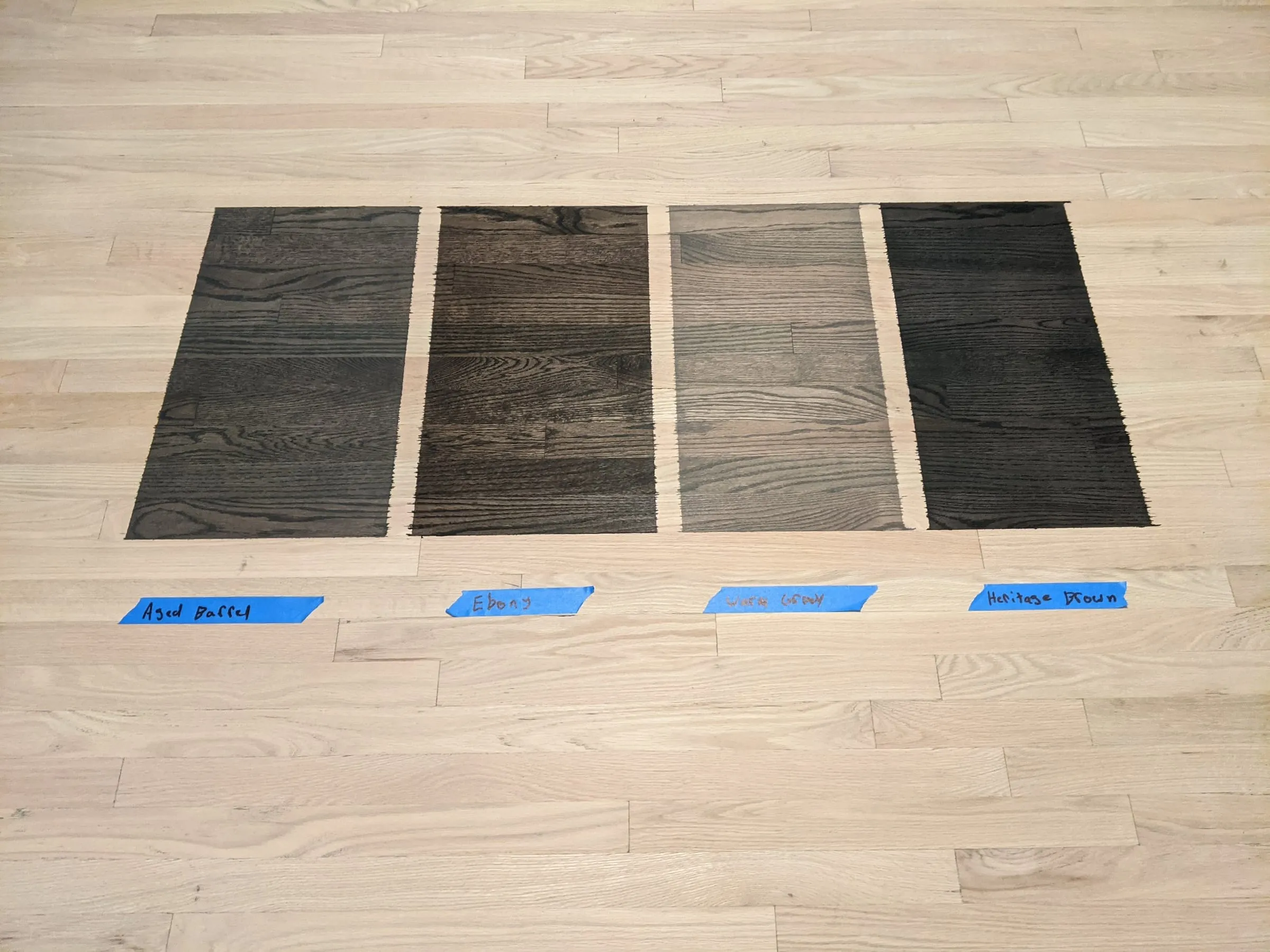 Four dark stain samples labeled on a sanded oak floor