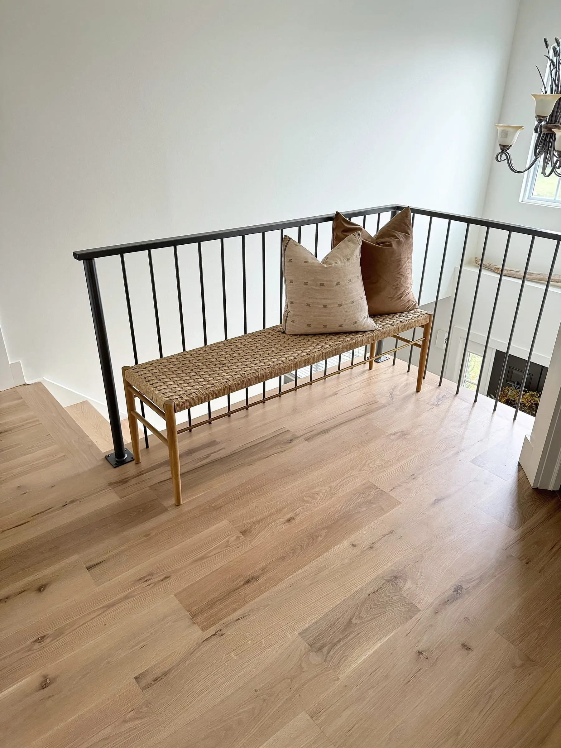 Light natural oak floor on an upstairs landing with a woven bench and black railing