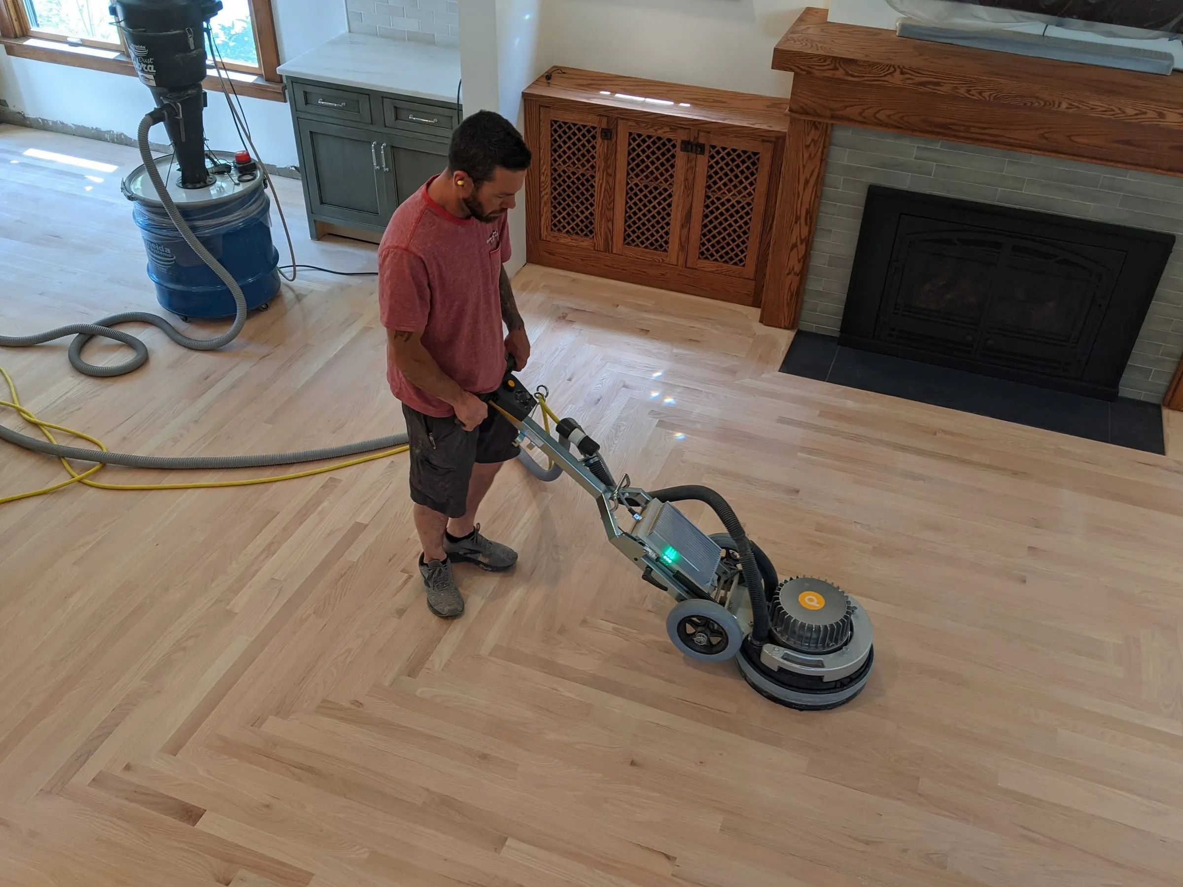 Technician sanding a light oak floor with a bordered pattern near a fireplace